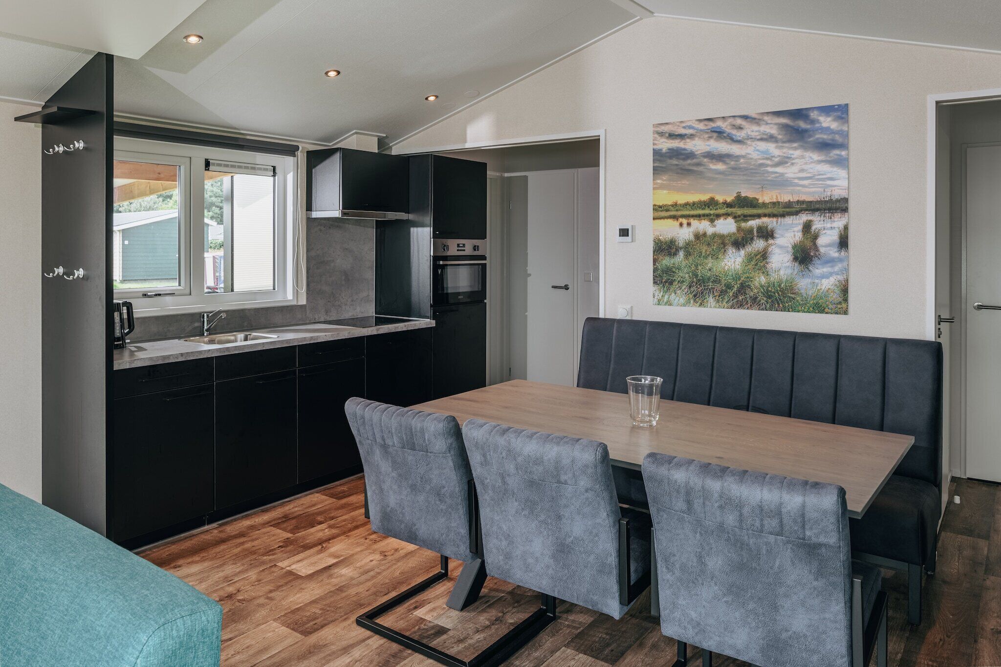 A compact kitchen with a dining area, a bench, and a painting of a landscape.