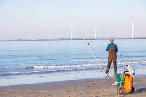 A beach with a person fishing, a tripod, and a cart with gear.