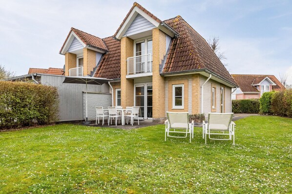 A two-story house with a brick exterior, a tiled roof, and a fenced backyard with a lawn and white outdoor furniture.