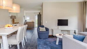 A modern living room with a dining area, a sofa, a TV, and a kitchen in the background. - Villa in Banjaard near Sandy North Sea Beach (Kamperland)