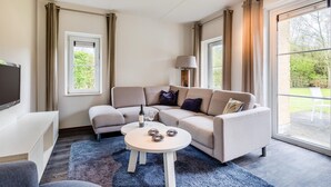 A modern living room with a beige sofa, a small round table, and a flat-screen TV. - Villa in Banjaard near Sandy North Sea Beach (Kamperland)