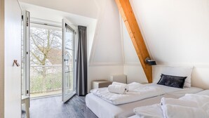 A bedroom with a large window, a bed with white linens, a wooden ceiling beam, and a small bedside table. - Villa in Banjaard near Sandy North Sea Beach (Kamperland)