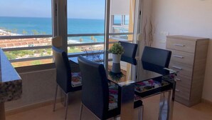 Un balcón con vista al océano, una mesa de comedor con sillas, una planta pequeña y un armario de madera.