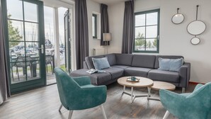 A modern living room with a grey sectional sofa, teal armchairs, a round coffee table, and large windows offering a view of a marina. - Cozy Volendam Getaway (Volendam)