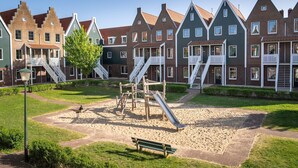 A playground with slides and a bench, surrounded by traditional houses with steep roofs and white railings. - Lakeside Villa in Volendam (Volendam)