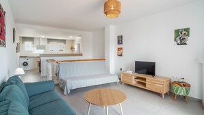 A modern living room with a sofa, a coffee table, a TV, and a kitchen in the background.