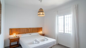 A neatly arranged hotel room with a bed, bedside tables, a hanging lamp, and a window with curtains.