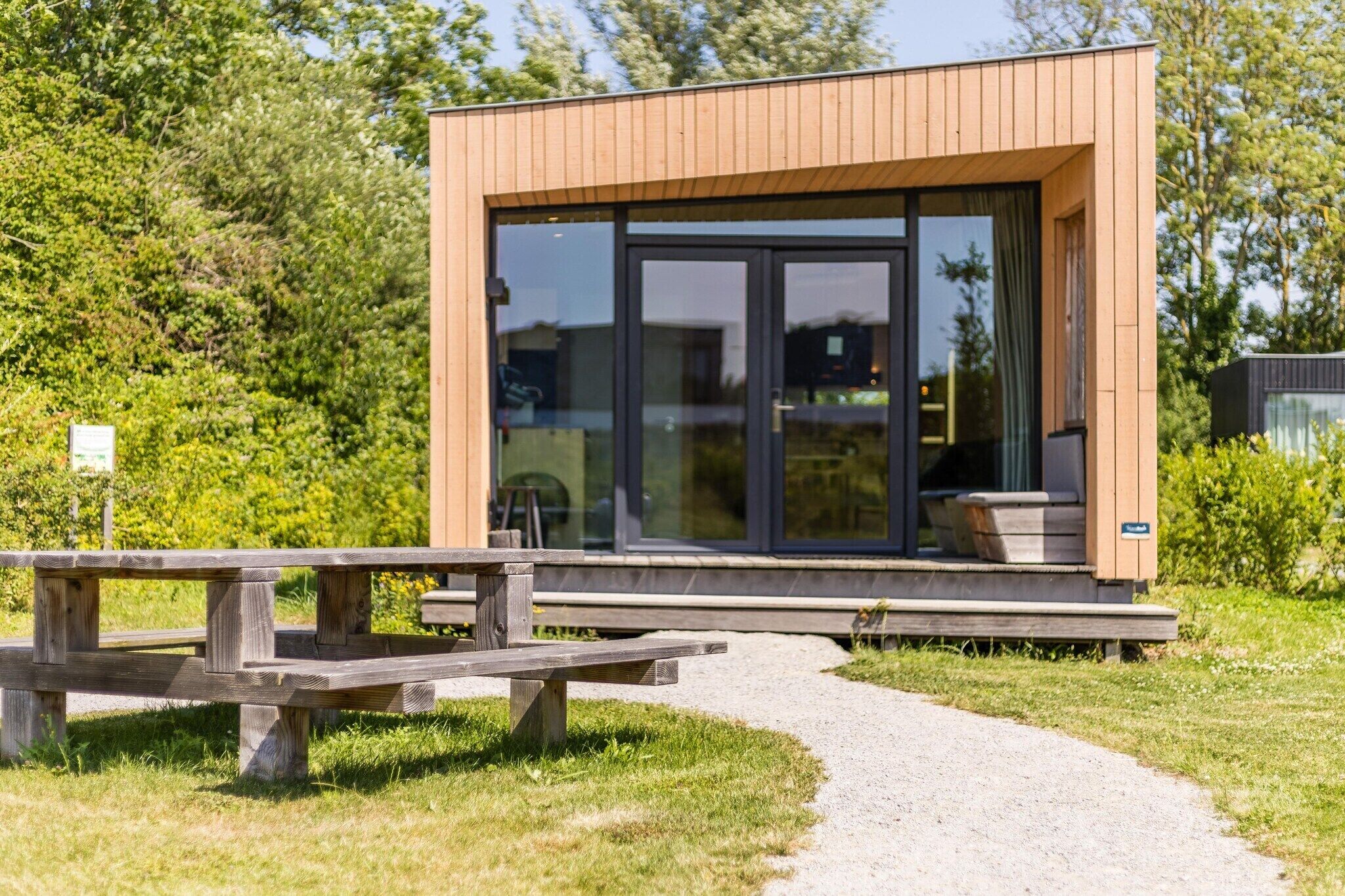A modern building with large glass windows, a wooden exterior, and a gravel path leading to a wooden bench.