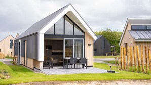 A modern house with a large glass window, a patio with a table and chairs, and a wooden fence in the background.