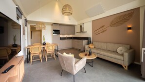 A modern living room with a sofa, dining table, and chairs. There is a kitchen area with cabinets and a microwave.