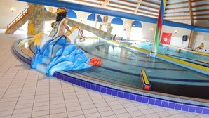 An indoor swimming pool with a large decorative sculpture, a diving platform, and a flag on the wall.