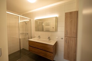 Un baño moderno con cabina de ducha de vidrio, un tocador de madera con espejo y un armario de madera.