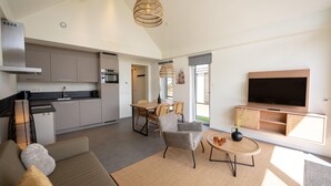A modern kitchen with grey cabinets, a built-in oven, and a dining area with a table and chairs. There's a flat-screen TV mounted on the wall and a sofa with a coffee table in the living area. - Modern Lodge by the Water (Breskens)