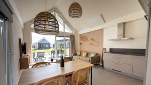 A modern kitchen with white cabinets, a wooden dining table, wicker chairs, and a large window offering a view of the outside. - Modern Lodge by the Water (Breskens)