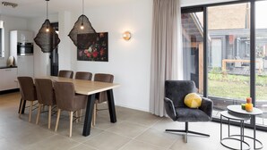 A modern dining area with a wooden table and chairs, a black upholstered armchair, and a small round table with candles.