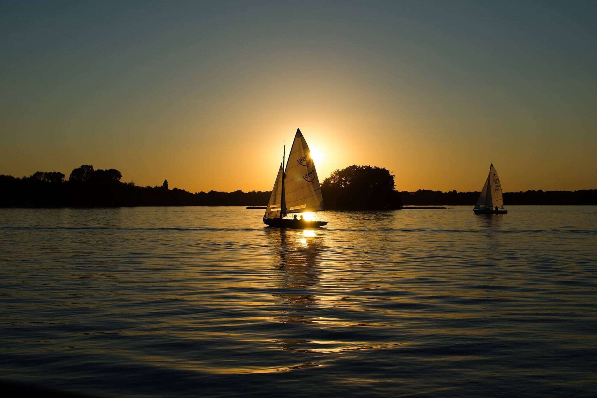 A sunset over a calm body of water with two sailboats.