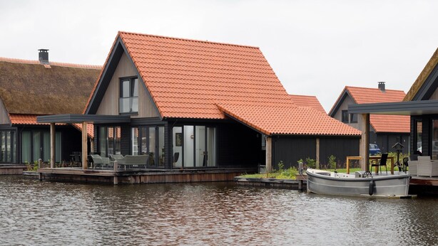 A waterfront property with a boat dock, a covered outdoor seating area, and a building with a red-tiled roof.