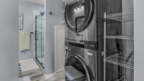 A laundry room with two stacked washers and dryers, a glass shower enclosure, and a white towel on the floor. - Black Bear Cabin - Fire pit - grill- view- pets-fireplace-king bed-wifi-gameroom (Berkeley Springs)