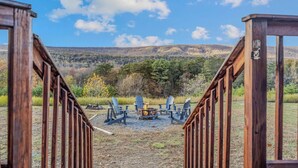 A wooden deck leading to a seating area with Adirondack chairs and a fire pit, overlooking a forested hillside. - Black Bear Cabin - Fire pit - grill- view- pets-fireplace-king bed-wifi-gameroom (Berkeley Springs)
