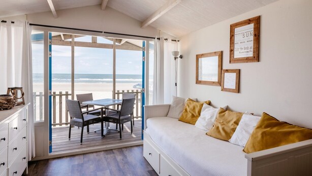 A room with a bed, a table with chairs, and a view of the beach.