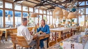 A restaurant with large windows, wicker furniture, and hanging rattan lamps.