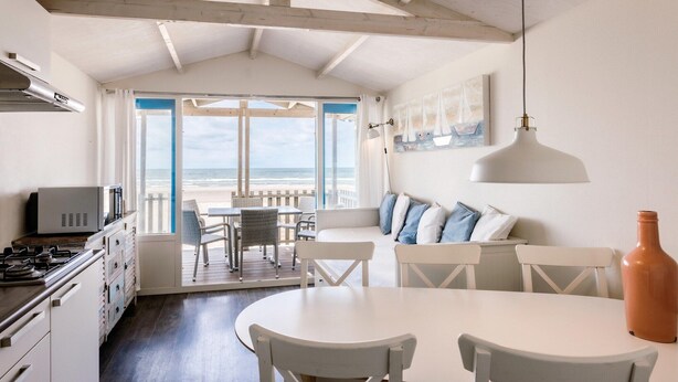 A kitchen with white cabinets, a stove, and a dining area with a white table and chairs. There is a large window with a view of the beach. - Beach House in Wijk aan Zee with Sea View (Wijk aan Zee)