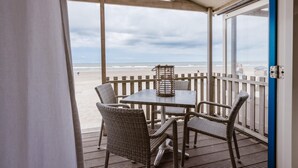 A covered outdoor seating area with wicker chairs and a table, overlooking a beach. - Beach House in Wijk aan Zee with Sea View (Wijk aan Zee)