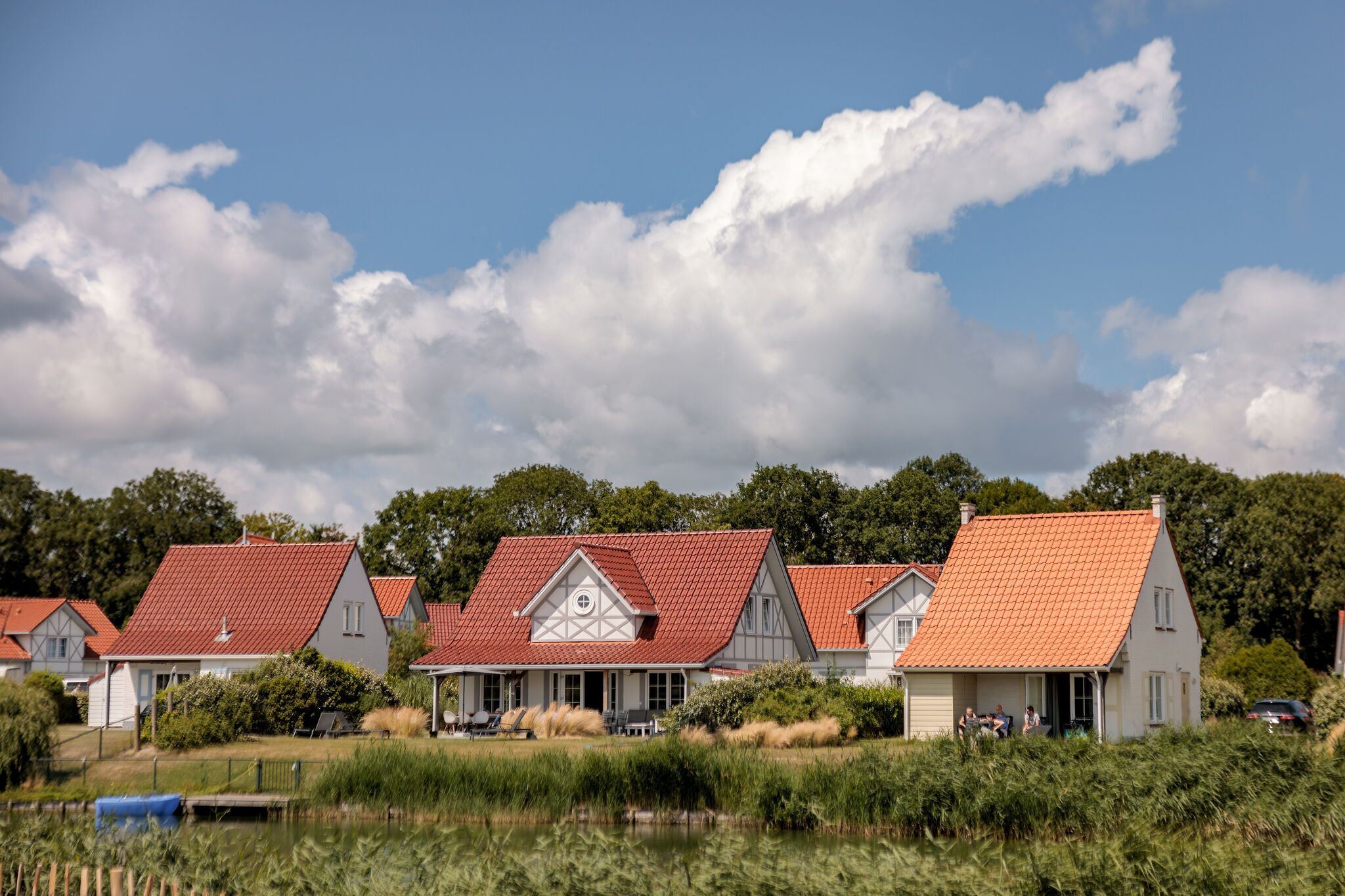 Une rangée de maisons traditionnelles aux toits de tuiles rouges, situées au bord d’un plan d’eau, sous un ciel dégagé.