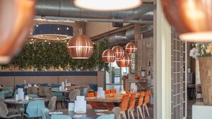 Ein modernes Restaurant mit runden Tischen, orangefarbenen Stühlen und Pendelleuchten aus Kupfer.