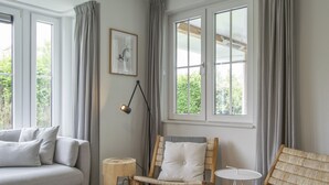 Ein Zimmer mit einer Couch, zwei Korbstühlen, einem kleinen runden Tisch und einer Stehlampe.