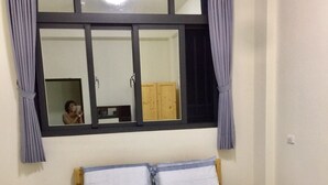 Een eenpersoonsbed met houten frame en een lichtkleurig matras, een raam met gordijnen, en een houten garderobe.