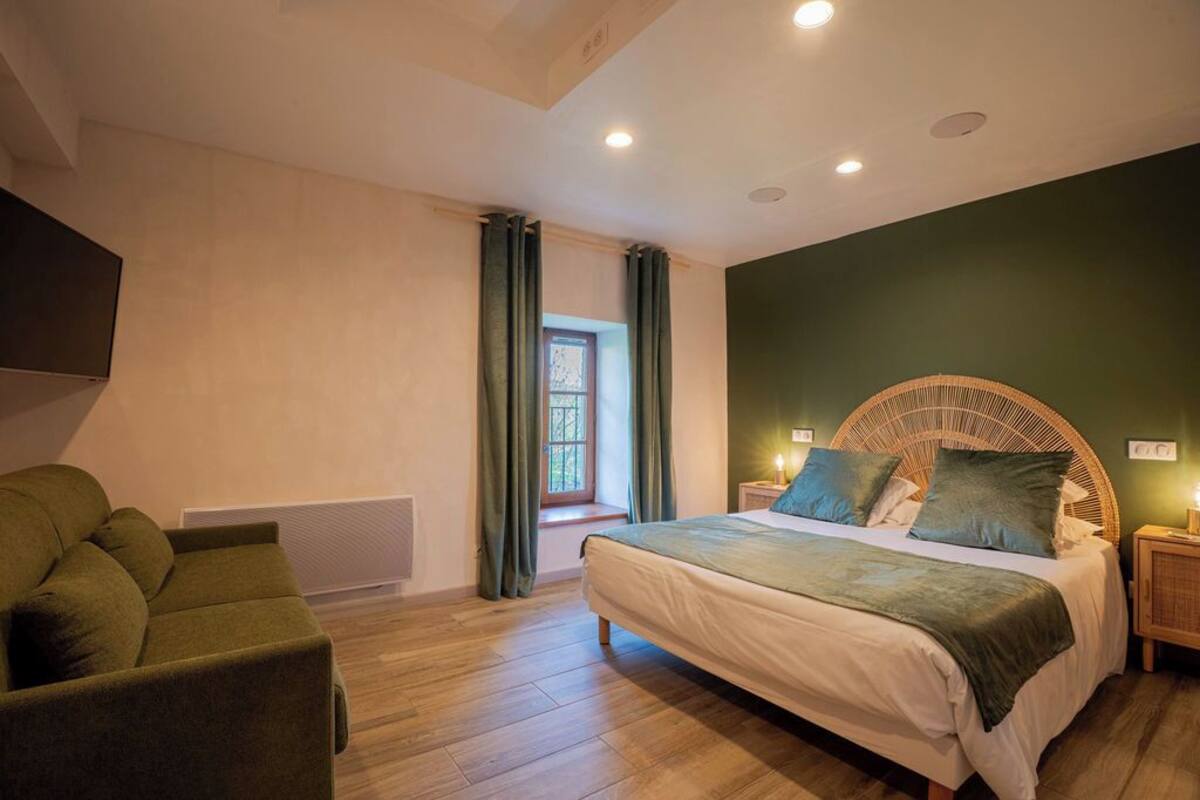 Une chambre à coucher avec un lit, une chaise, une fenêtre avec des rideaux et un téléviseur fixé au mur.