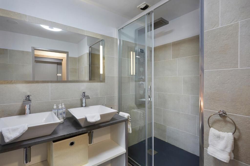 Een moderne badkamer met twee wastafels, een douchecabine van glas en een handdoekrek.