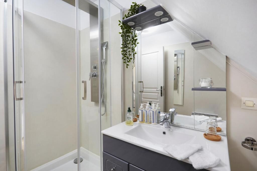 A modern bathroom with a glass shower enclosure, a white sink with toiletries, and a mirror above the vanity.