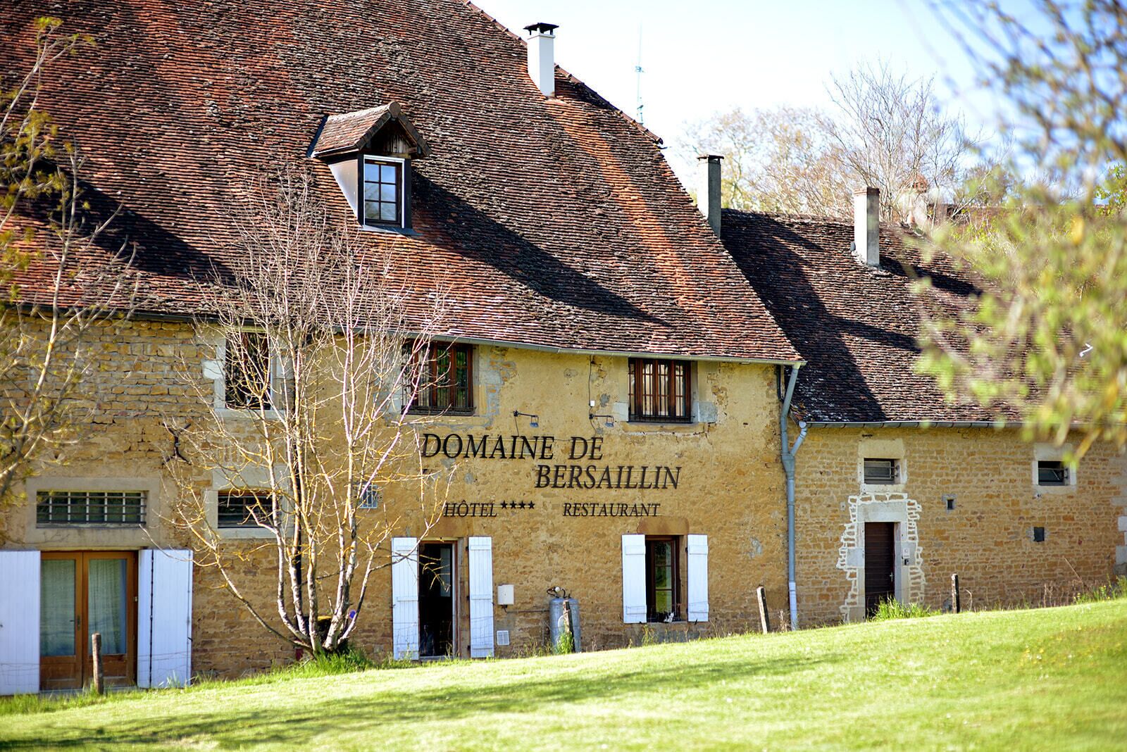 Een gebouw met twee verdiepingen, een gevel van natuursteen, een bord met daarop 'Domaine de Besailin HOTEL RESTAURANT' en een schuin dak.