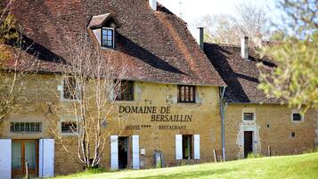 Een gebouw met twee verdiepingen, een gevel van natuursteen, een bord met daarop 'Domaine de Besailin HOTEL RESTAURANT' en een schuin dak.