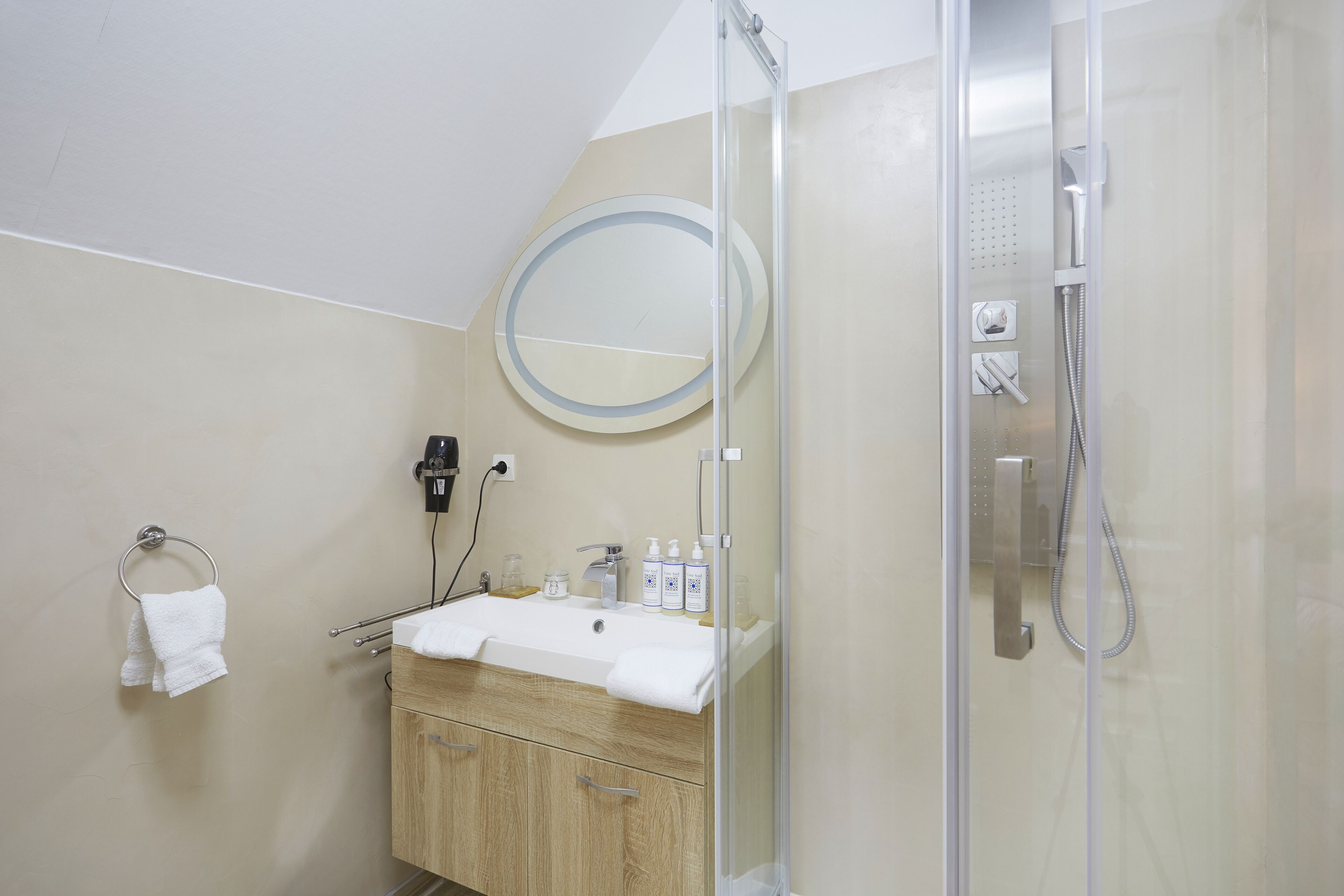 Een badkamer met een douche met glazen wand, een wastafel met spiegel erboven en een handdoekrek met witte handdoeken.