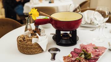 Une table à manger avec un caquelon à fondue, un panier de pain, une assiette de charcuterie et un verre à vin.