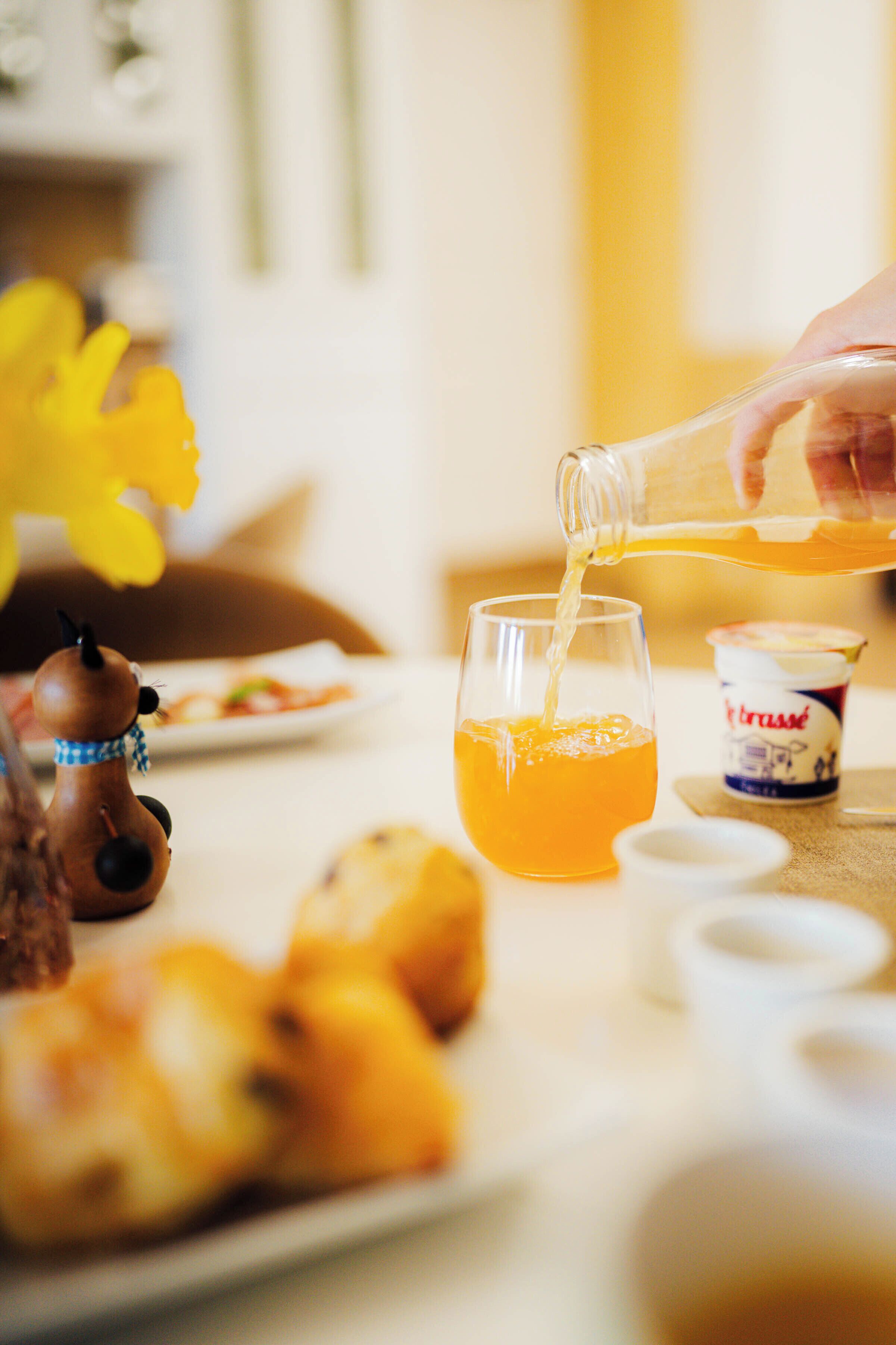 A table with a glass of orange liquid, a small container, and a decorative item.