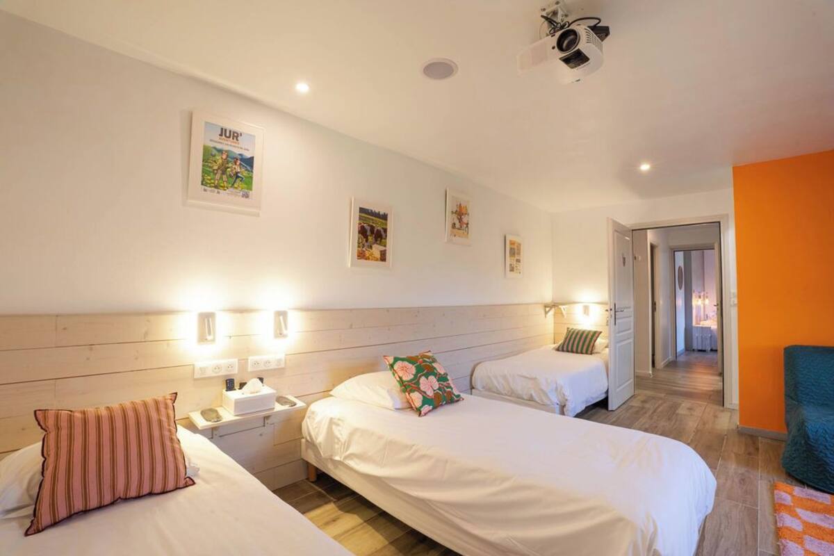 Une chambre d’hôtel avec deux lits, une tête de lit en bois, des lampes fixées au mur et un projecteur.