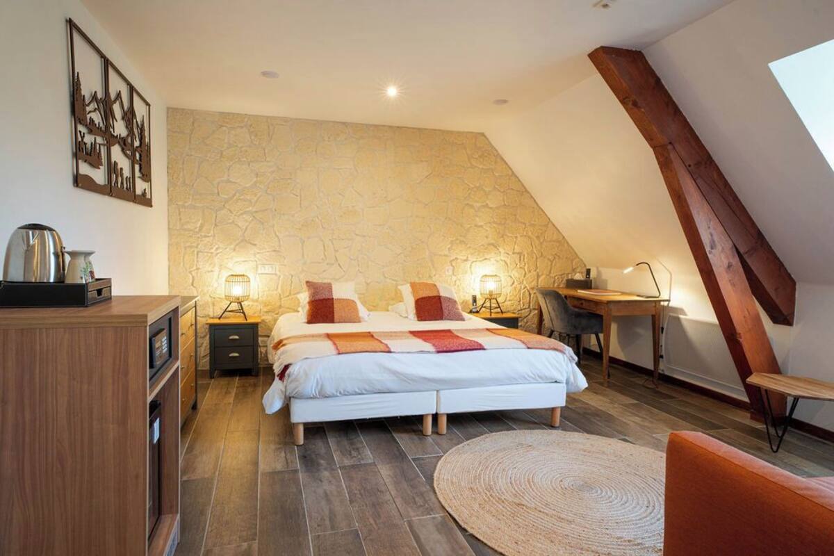 Une chambre avec un mur en pierre, un lit, des tables de chevet, un bureau et une chaise.