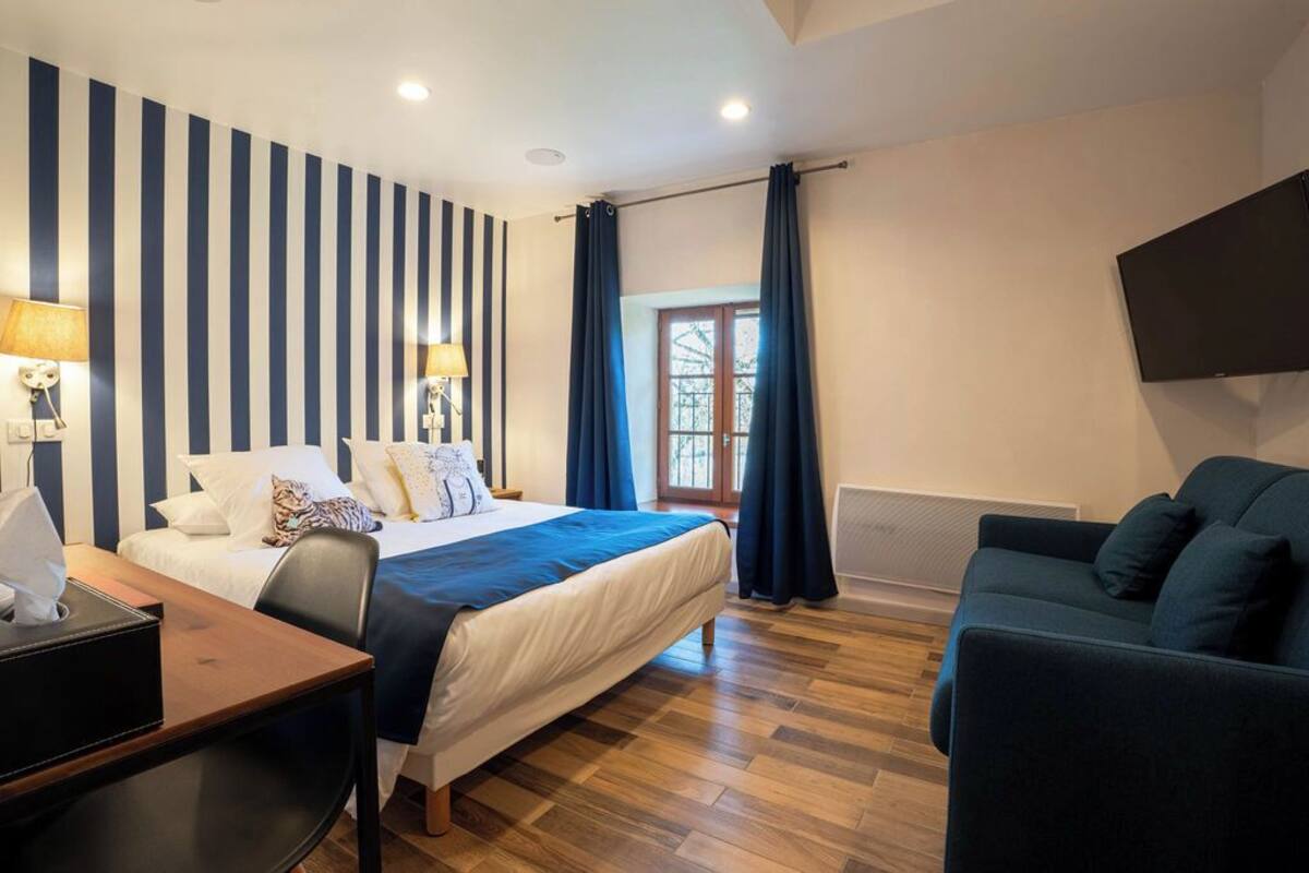 Une chambre d’hôtel équipée d’un lit, d’un bureau, d’une chaise, d’un canapé, d’une télévision et d’une fenêtre avec des rideaux.