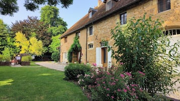 A stone building with a garden, a small outdoor seating area, and a pathway leading to the entrance.