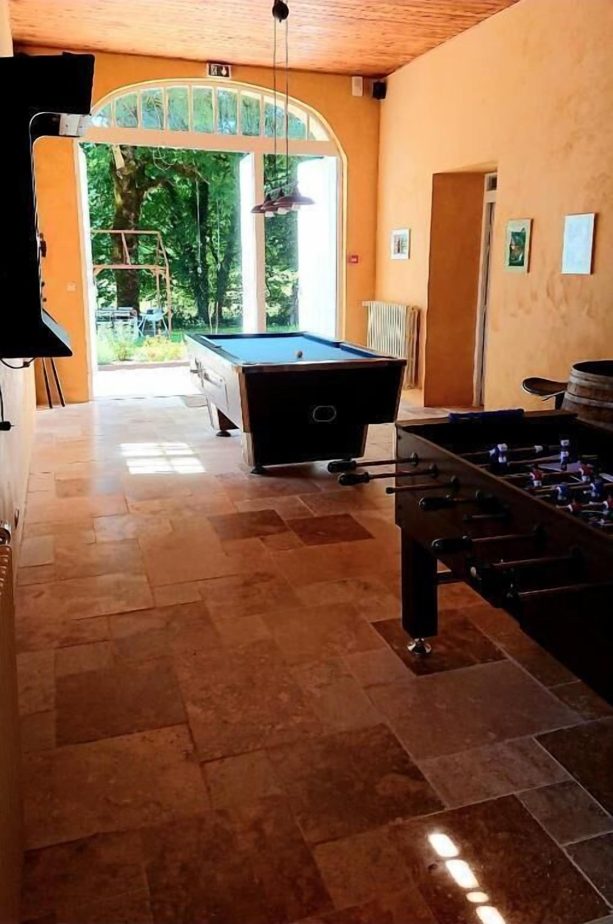 Una sala de billar con mesa de billar y mesa de fútbol, televisor y vistas al exterior.