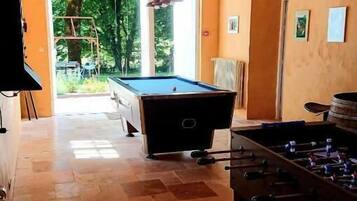 Una sala de billar con mesa de billar y mesa de fútbol, televisor y vistas al exterior.