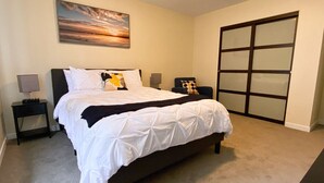 Une chambre à coucher comprenant un lit, deux tables de chevet, un tableau accroché au mur et une porte coulissante.