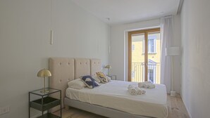 Une chambre moderne avec un grand lit, une table de chevet avec une lampe et une vue sur le balcon extérieur.