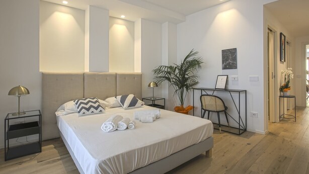 Une chambre d’hôtel moderne avec un grand lit, des tables de chevet, un bureau et une plante en pot.