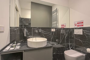 A modern bathroom with a white sink, black marble tiles, a toilet, and a mirror. - Milan Chic Suite 6 (Milan)
