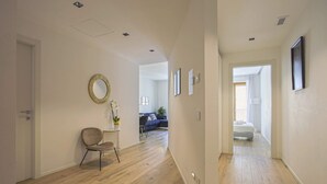 Un couloir avec un plancher en bois, un miroir rond accroché au mur et une chaise.
